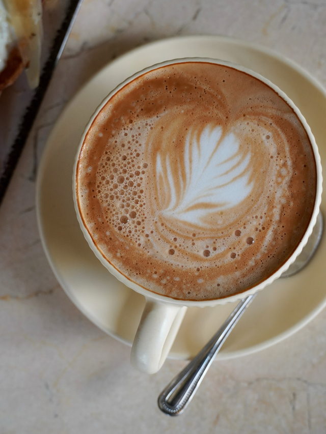 A cappuccino from above, a leaf drawn into the foam, on a cream saucer.