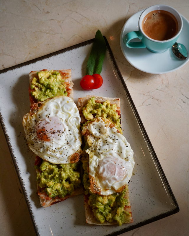 Crushed avocado and fried eggs on slabs of focaccia, with an espresso in a pale blue cup.
