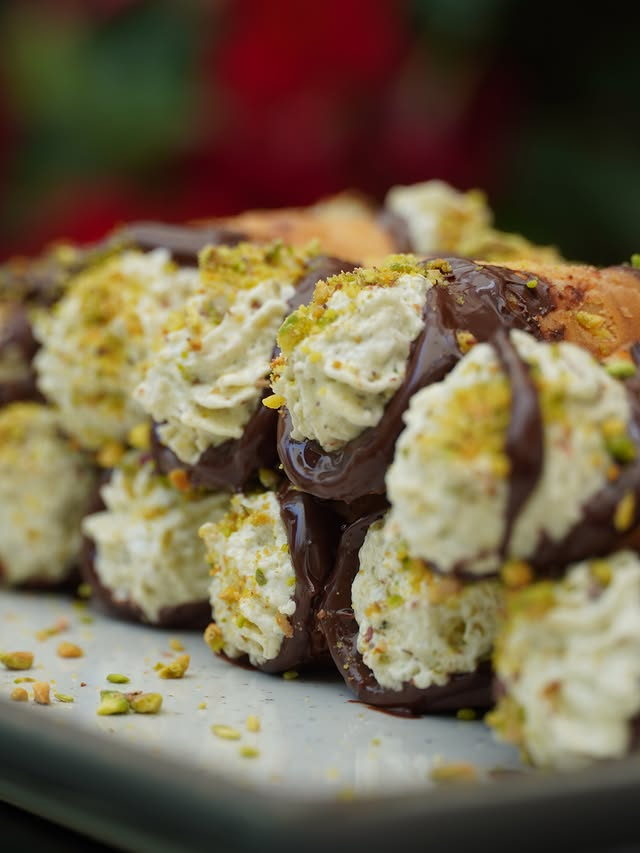 Cannoli piped with ricotta cream, dipped in dark chocolate and scattered with crushed pistachio.