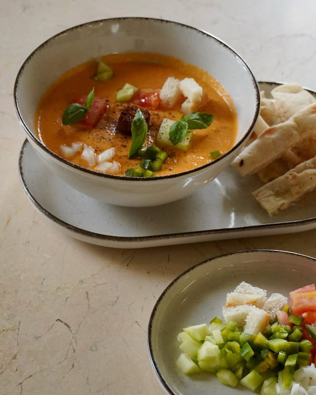 A bowl of chilled gazpacho topped with diced vegetables and basil, with bread alongside.