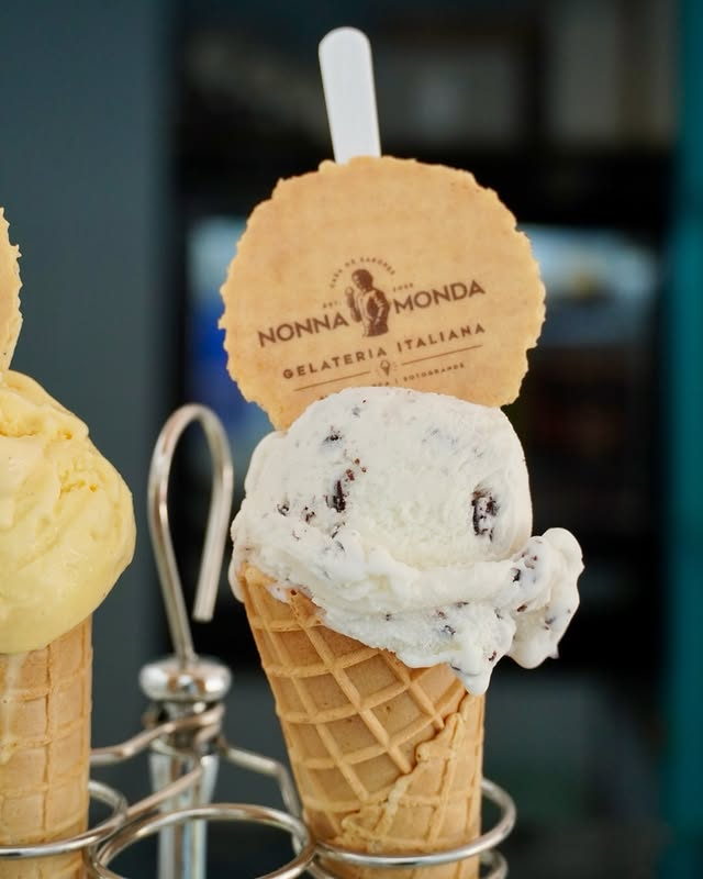 Two gelato cones in a stand, one stracciatella with a round Nonna Monda wafer standing in it.