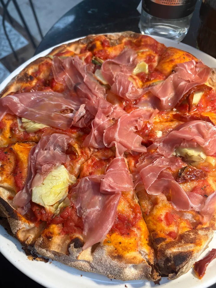 A thin, blistered pizza draped with prosciutto and artichoke hearts.