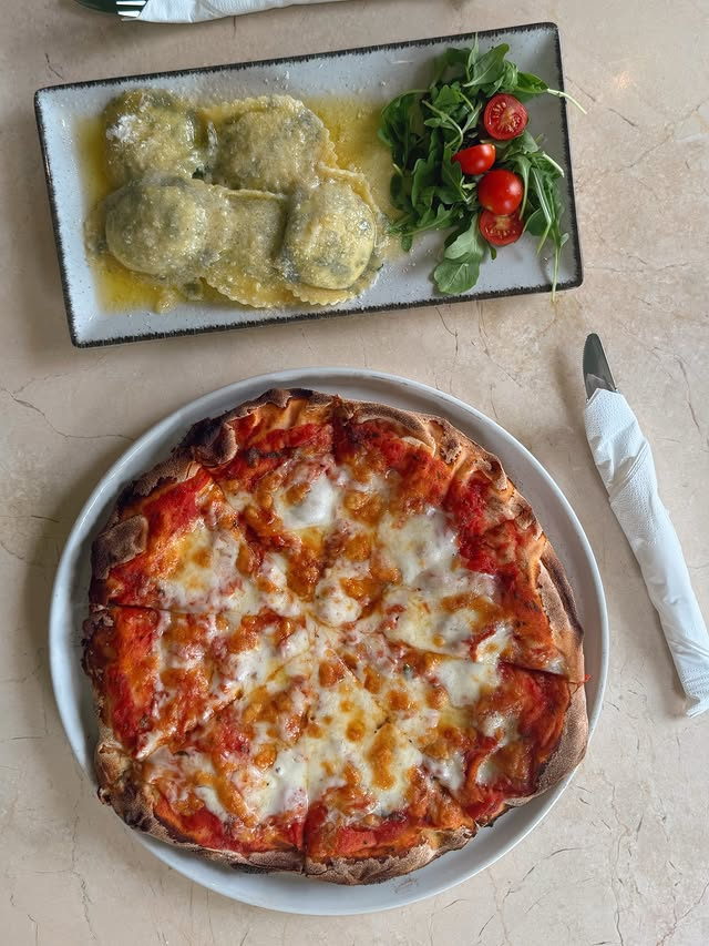 A margherita pizza and a plate of spinach ravioli with rocket and tomatoes.