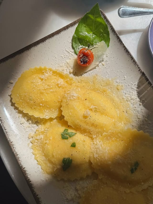 Ravioli dressed in butter and sage under a drift of grated parmesan, on a speckled plate.
