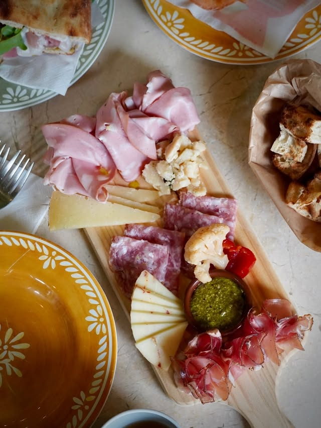 A wooden board of mortadella, salami, coppa and cheeses with pesto and crostini.