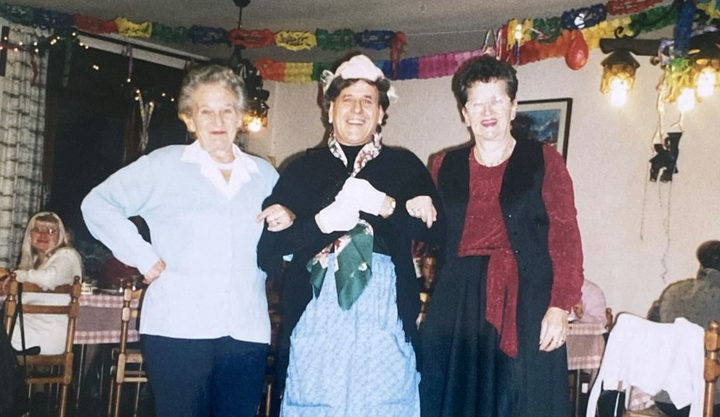 Three women at a village party, paper bunting strung across the ceiling.