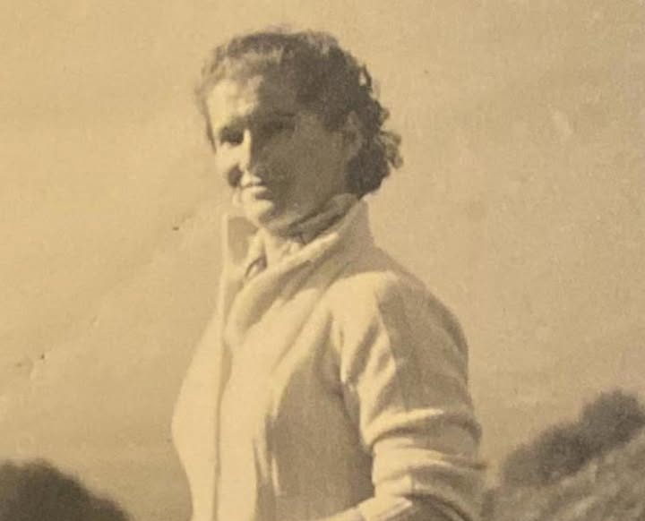 A sepia photograph of a young woman outdoors in the hills, hair blown back, half smiling at the camera.