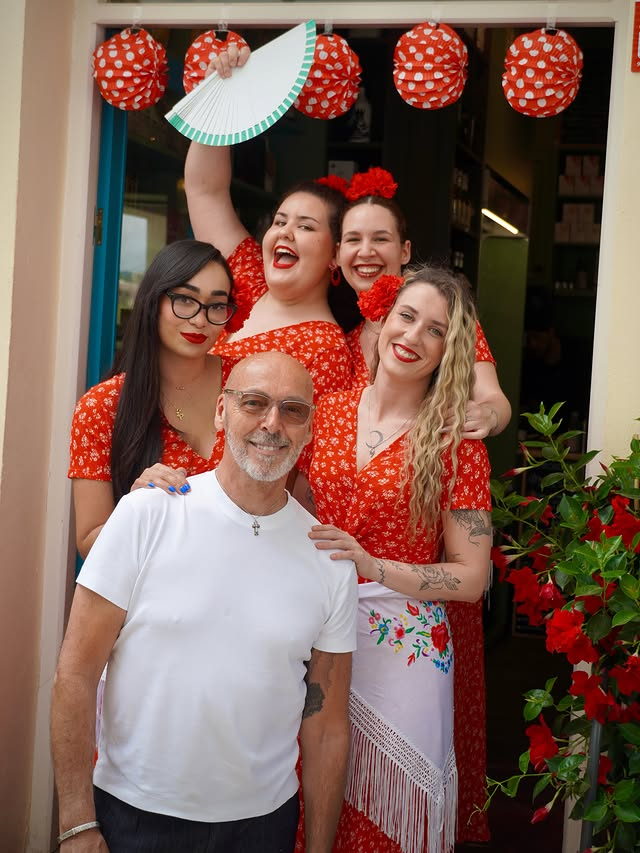 Peter with the team in red flamenco dresses in the doorway during feria, red lanterns above.