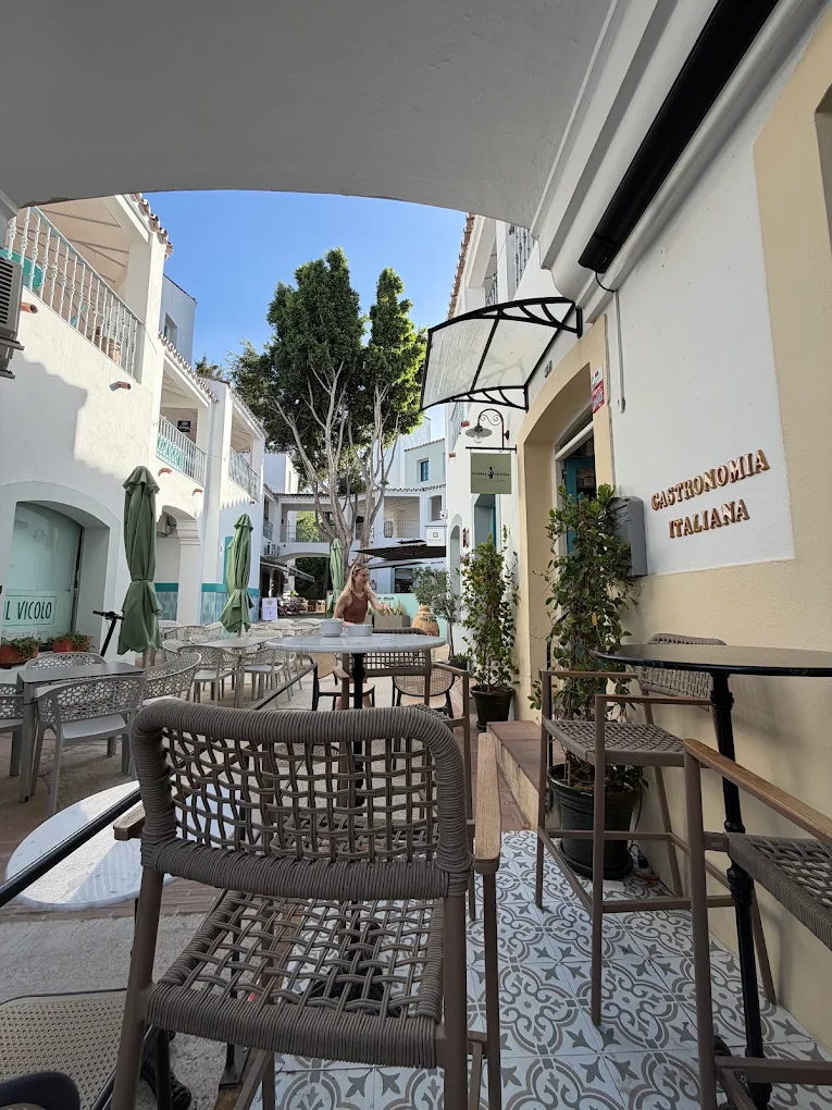 Tables under the awning outside Nonna Monda, looking down the whitewashed lane of Plaza Blanca, with GASTRONOMIA ITALIANA lettering on the wall.
