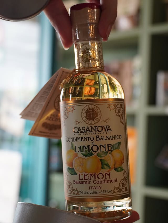 A hand holding a bottle of Casanova lemon balsamic condiment, its label painted with lemons.