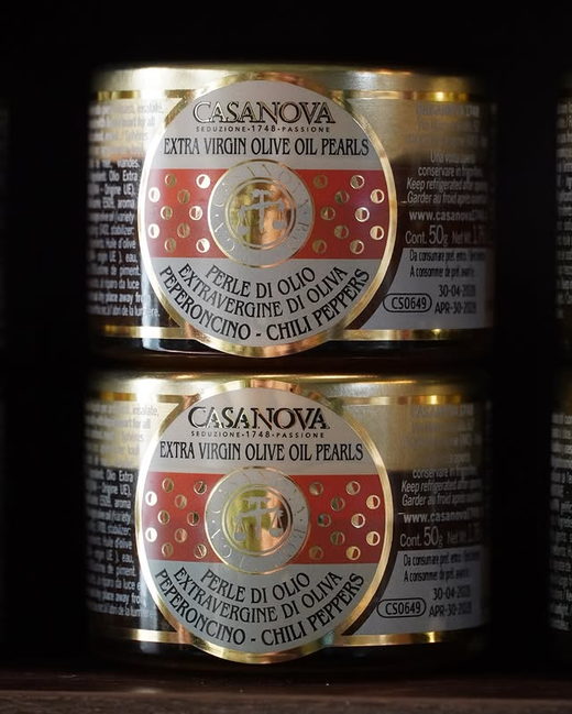 Tins of olive oil pearls with chilli, their labels banded in red.