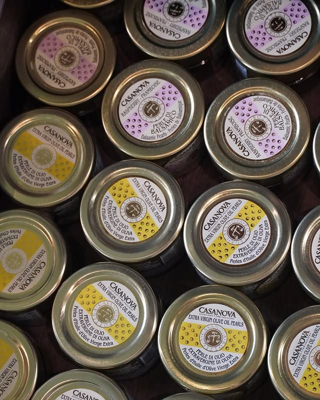 Rows of small gold tins of olive oil and balsamic pearls, seen from above.