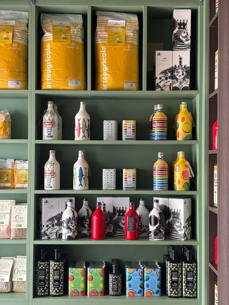 Sage-green shelves stacked with hand-painted olive oil bottles, flour from Puglia, dried pulses and tinned oils.
