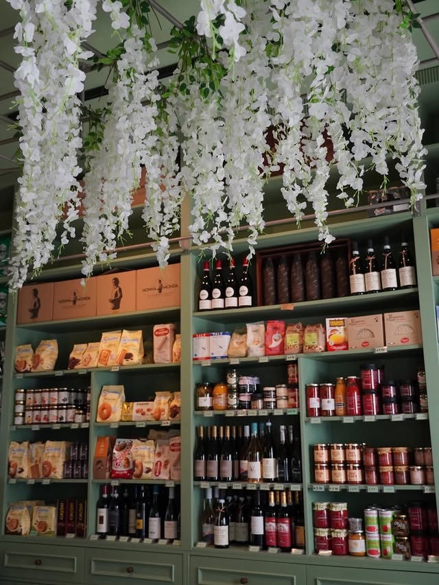 Floor-to-ceiling sage shelves of wine, preserves, biscuits and dried pasta, with white wisteria hanging from the ceiling.